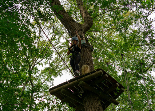 Young woman stepping forward on treetop platform in adventure park