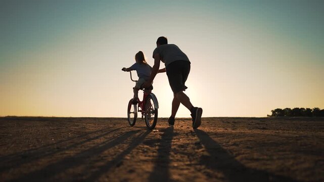 Happy family. Father teaches daughter to ride bike in park. father helps his daughter in her studies. happy child dreams of traveling by bike. child is learning to ride bike.