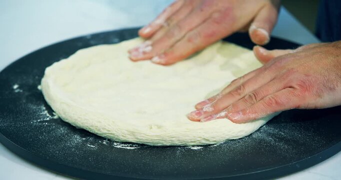 Adult man's hands flattening out pizza dough, closeup