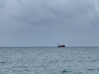 Fototapeta premium Fishing vessel at sea on a cloudy day, bobbing gently in the water