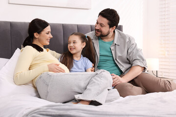 Obraz premium Pregnant woman, her husband and daughter on bed at home
