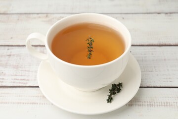 Aromatic thyme tea in cup on light wooden table, closeup