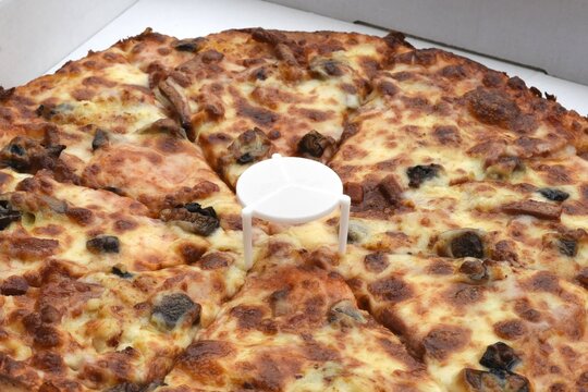Photo of pizza in a cardboard box with plastic white saver.