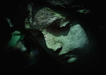 Naklejka premium Dark stone face emerging from shadow, symbol of inner pain, silence, and emotional collapse.