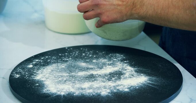 Cook removing pizza dough from plastic container and spreading flour on platform - closeup shot