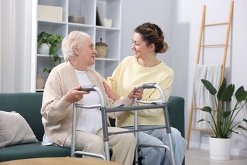 Fototapeta premium Caregiver helping senior woman with walker indoors