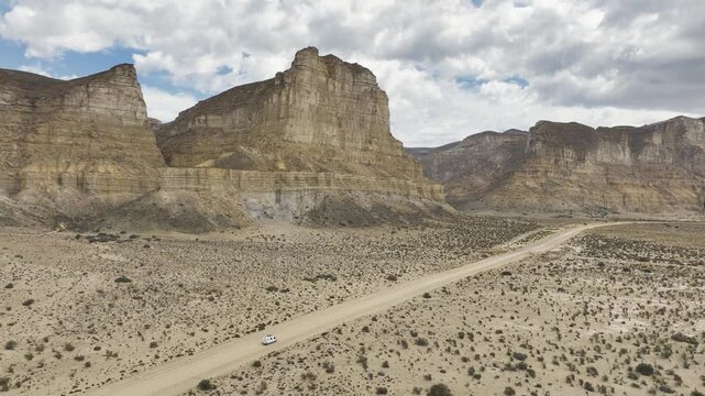 Aerial view of a small van driving on a remote dirt road through the arid landscape of the Patagonian steppe, Chubut, Argentina