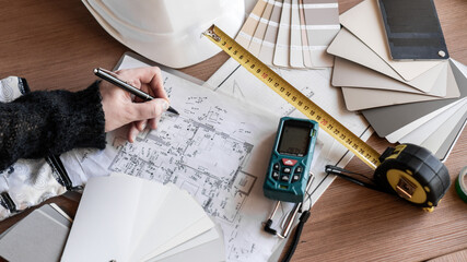 female interior designer writes down apartment measurements and makes drawings. plan, construction diagrams on the table. catalog, tape measure, laser, ruler and pen, construction helmet © drk.muse