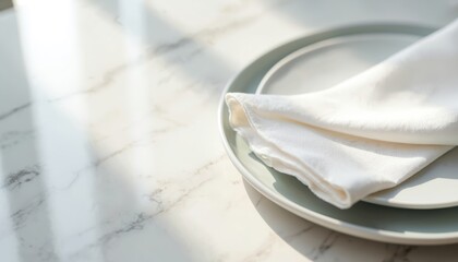 White fabric napkin folded neatly atop grey plate on marble table. Natural light creates soft shadows, suggesting clean elegance for dining or decor.