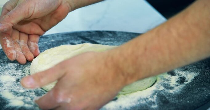 Hands of cook padding down flour covered pizza dough - closeup