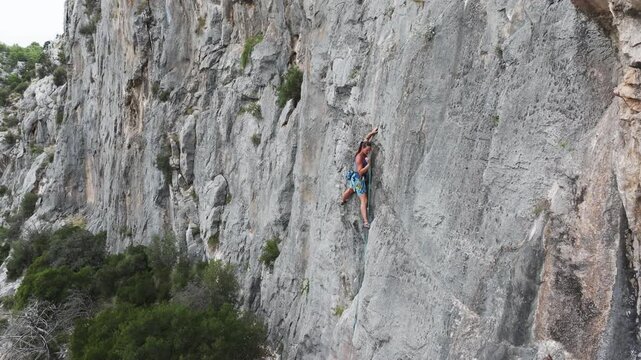 AERIAL, CLOSE UP: While lead climbing a vertical limestone wall, female athlete in blue top attaches a quickdraw and clips a rope. Movement and dramatic verticality of the Hvar island climbing routes.