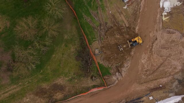Construction Work Beside Flooded Terrain: An aerial view shows a yellow excavator performing construction work near a flooded area with muddy water and debris, highlighting disaster response efforts.