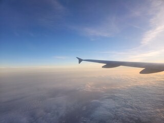 Fototapeta premium A calm airplane wing view at golden hour, gliding above a soft blanket of clouds under a warm, fading sunset sky