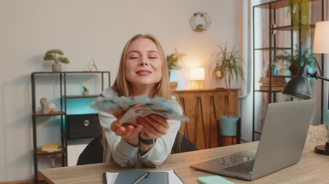 Businesswoman holding fan of cash money Ukrainian hryvnias UAH banknotes celebrate dance success career lottery jackpot game winner big income, wealth at home office workplace. Remote distant working.