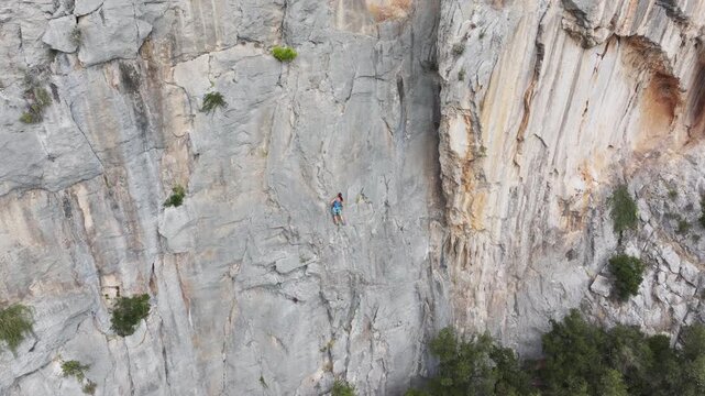 AERIAL: Female athlete navigating a complex limestone wall overlooking Mediterranean wilderness. Geological beauty of Dalmatian coast and solitude of sport climbing in a grand, natural environment.