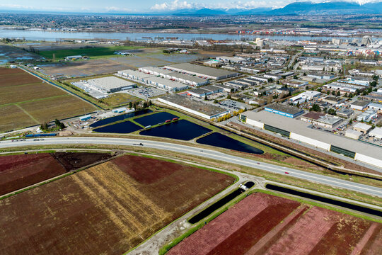 Canada, BC, Delta.  Area of light industry beside the Fraser River.  Agricultural land in the foreground with fields of cranberries.
