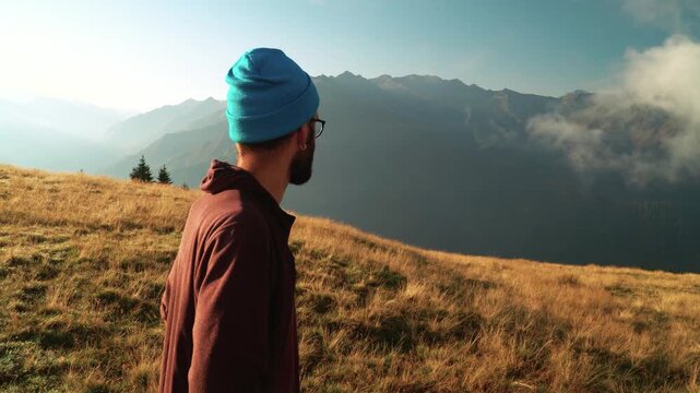 Bearded hipster in beanie hat and glasses overlooking mountain valley at sunrise
