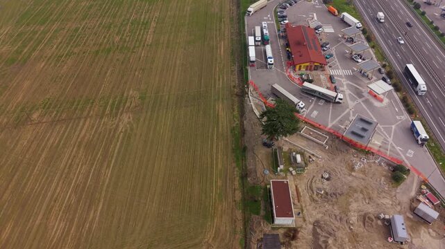 Roadside Rest Stop Panorama: An elevated view showcases a bustling roadside rest stop juxtaposed against a vast agricultural field, highlighting the intersection of human activity and the environment.