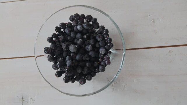 Cinematic slow motion movement from right to left across ripe blueberries in transparent bowl on wooden surface