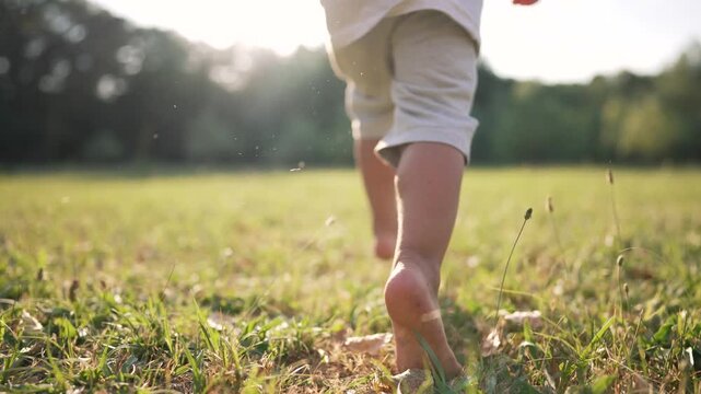 Happy kid runs barefoot on green young grass with pet. Happy family day. Healthy active lifestyle of child in park.