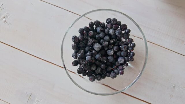Smooth slow motion lateral shot of frozen blueberries in glass bowl, natural fruit ingredient for healthy breakfast