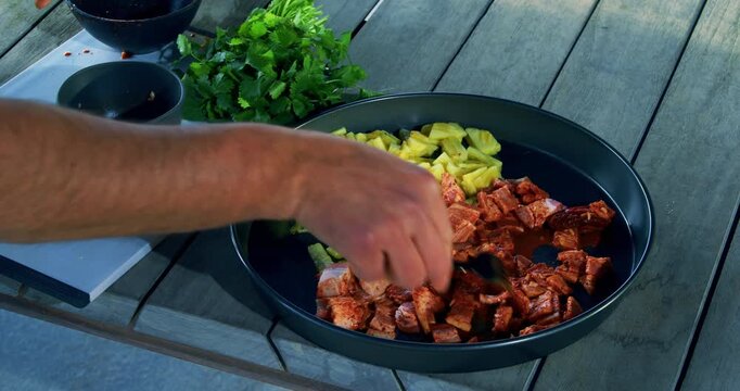 Slow zoom in on raw, chopped up food in pan as man's hand uses fork to spread it - closeup