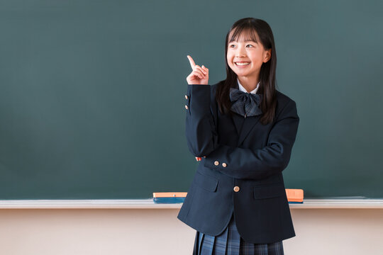 黒板の前に立ち笑顔でアイデアが思いつくブレザー姿の小学生,中学生,高校生の女子生徒