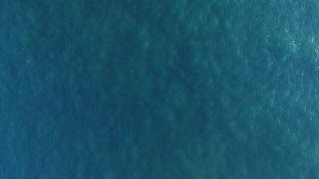 Aerial drone view capturing the smooth, endless surface of turquoise ocean water, subtle patterns and gentle ripples creating a minimalist, tranquil seascape that emphasizes texture, light, and