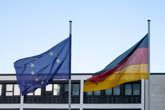 Europaflagge und Bundesflagge vor Geb&auml;ude und blauem Himmel