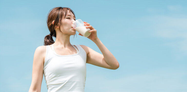 運動時にプロテイン・EAA・ドリンクを飲む女性(青空)