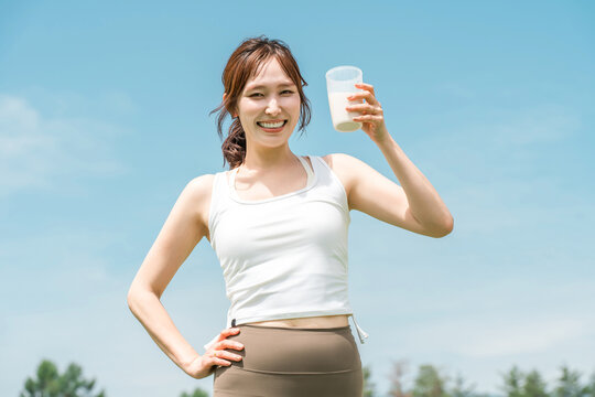 A woman drinking a protein/EAA drink during exercise (blue sky)