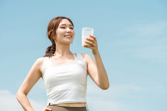 A woman drinking a protein/EAA drink during exercise (blue sky)