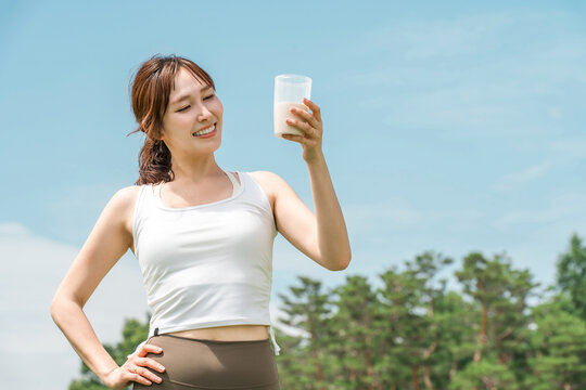 A woman drinking a protein/EAA drink during exercise (blue sky)