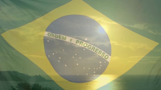 Brazilian flag appearing sheer over sea, sun rising causing ripples and flare showing shore glow