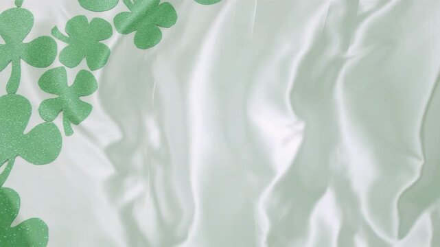 Pale mint satin folds shifting, soft light revealing green clovers growing into decorative border
