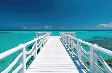 Fototapeta premium White wooden pier extends over bright turquoise ocean water under a clear blue sky. This tranquil tropical seascape evokes a sense of peace and perfect vacation.