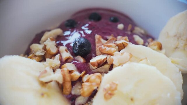 Macro slow motion placing fresh blueberries over walnuts and banana on oatmeal, vibrant healthy breakfast composition
