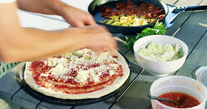 Close up of cook putting variety of toppings on pizza dough