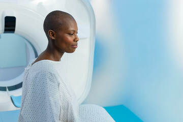 African American woman sitting on padded scanner table in radiology room wearing hospital gown
