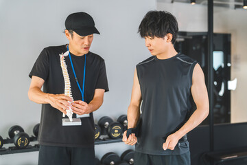 A trainer and a male gym member explaining using a skeletal specimen at a training gym