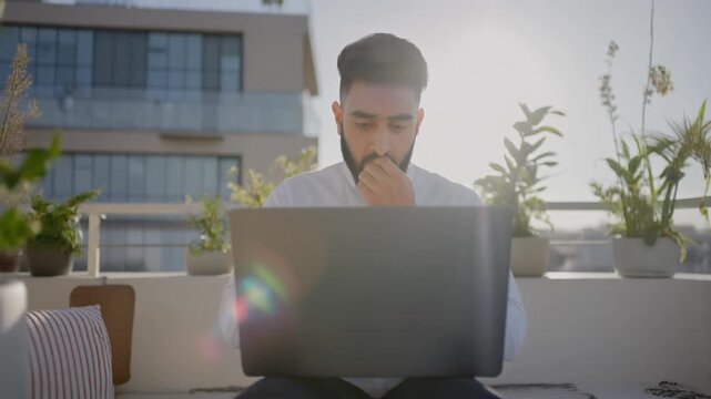 Man overwhelmed by digital workload on laptop outdoors in modern setting