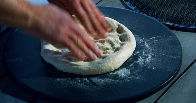 Adult man's fingers patting down flour covered pizza dough - closeup