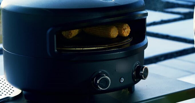 Corn on the cob rotating inside small oven with person nearby - closeup