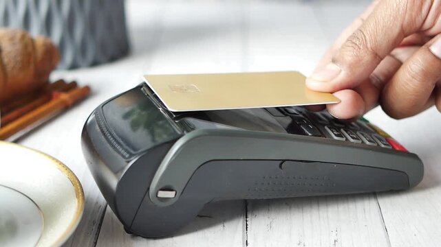 Person using contactless payment with credit card on pos machine in cafe