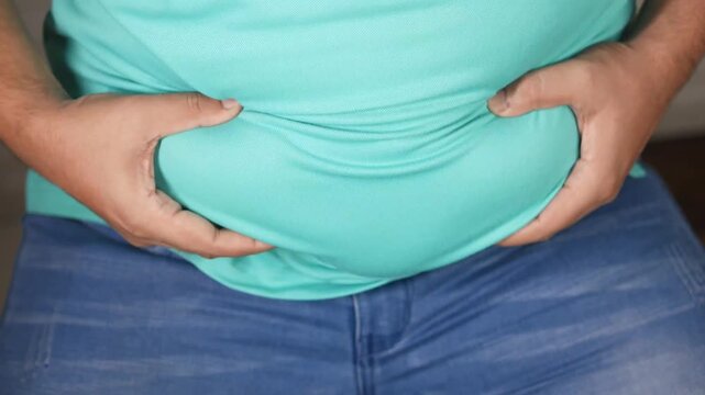 Man grabbing overweight belly showing bulge under t shirt and jeans, close up footage