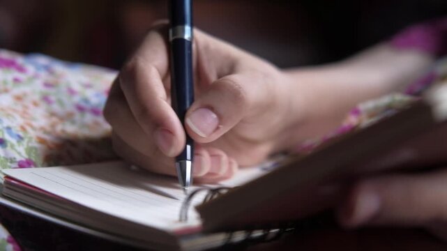 Close up hands of young person writing with pen in notebook, dynamic footage capturing student taking notes or journaling, personal reflection concept