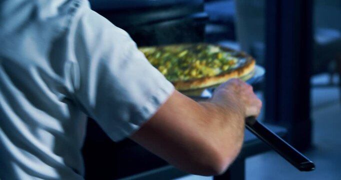 Cook using large spatula to place veggie pizza in small oven at dusk