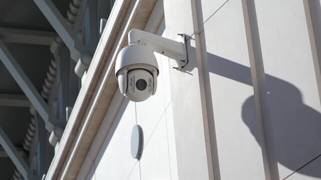 Outdoor white ptz security camera rotating on building wall for surveillance and safety monitoring