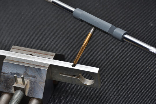 Threading tool in action on a aluminum piece. Tapping tool to create thread. Metal tap and drive handle. Hand threading tool.