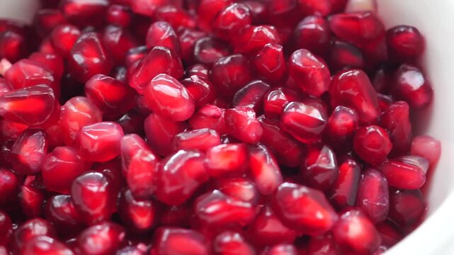 Close-up footage of fresh pomegranate seeds glistening in white bowl, healthy food background